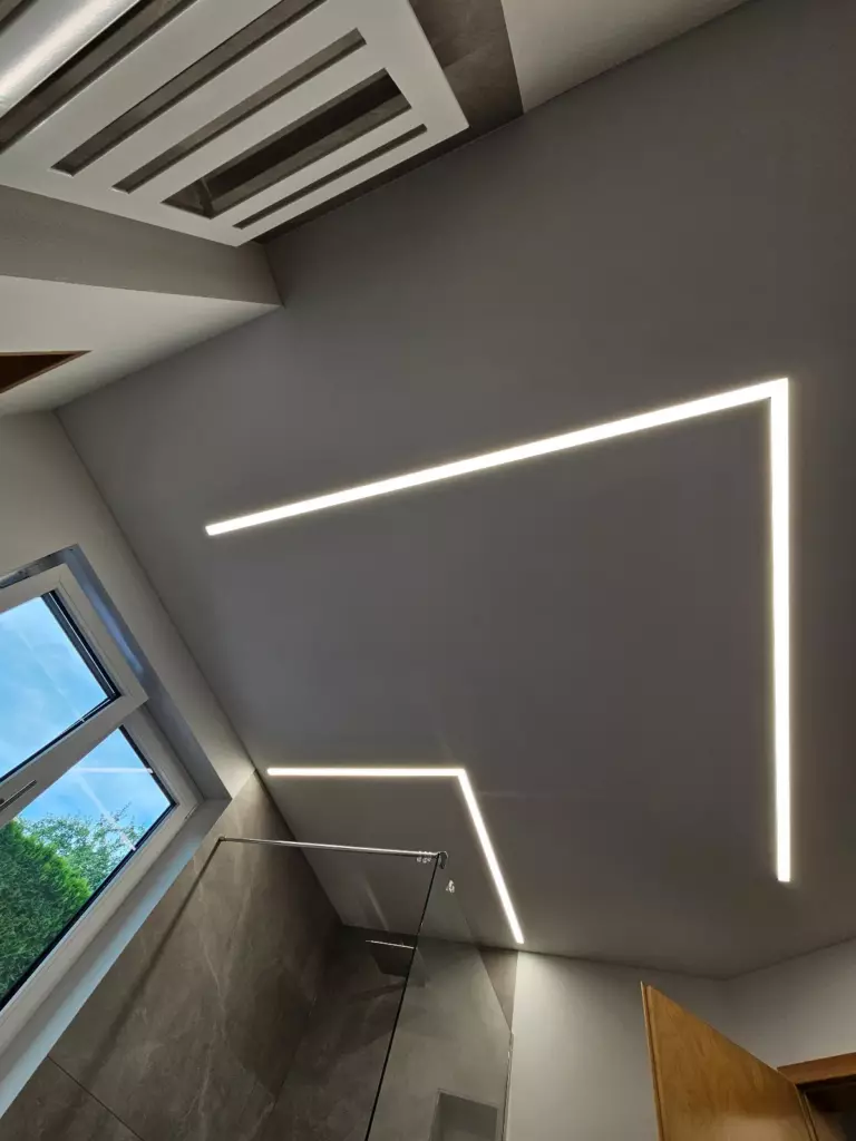 Blick nach oben: LED-Lichtlinien bilden zwei rechte Winkel in der Spanndecke über der Dusche