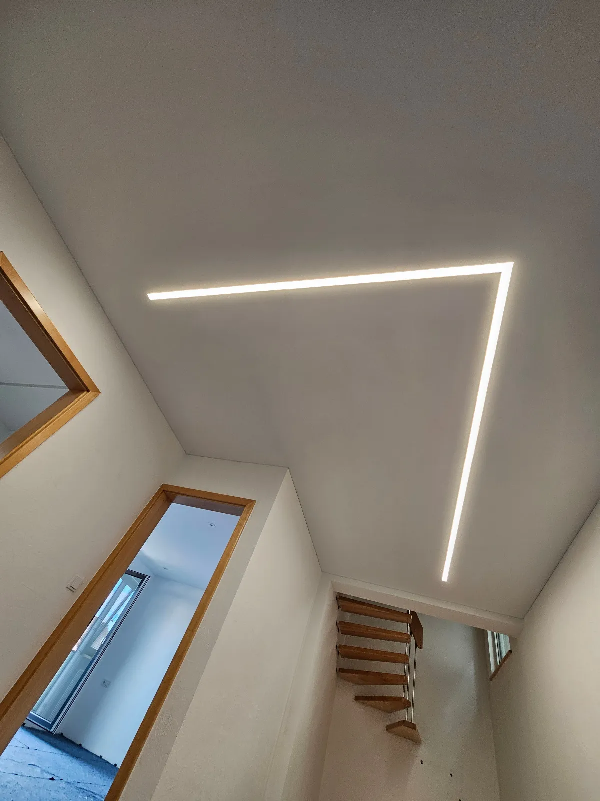 Hochformat: winkelförmige LED-Lichtlinie in der Flurdecke über Türen und Treppe